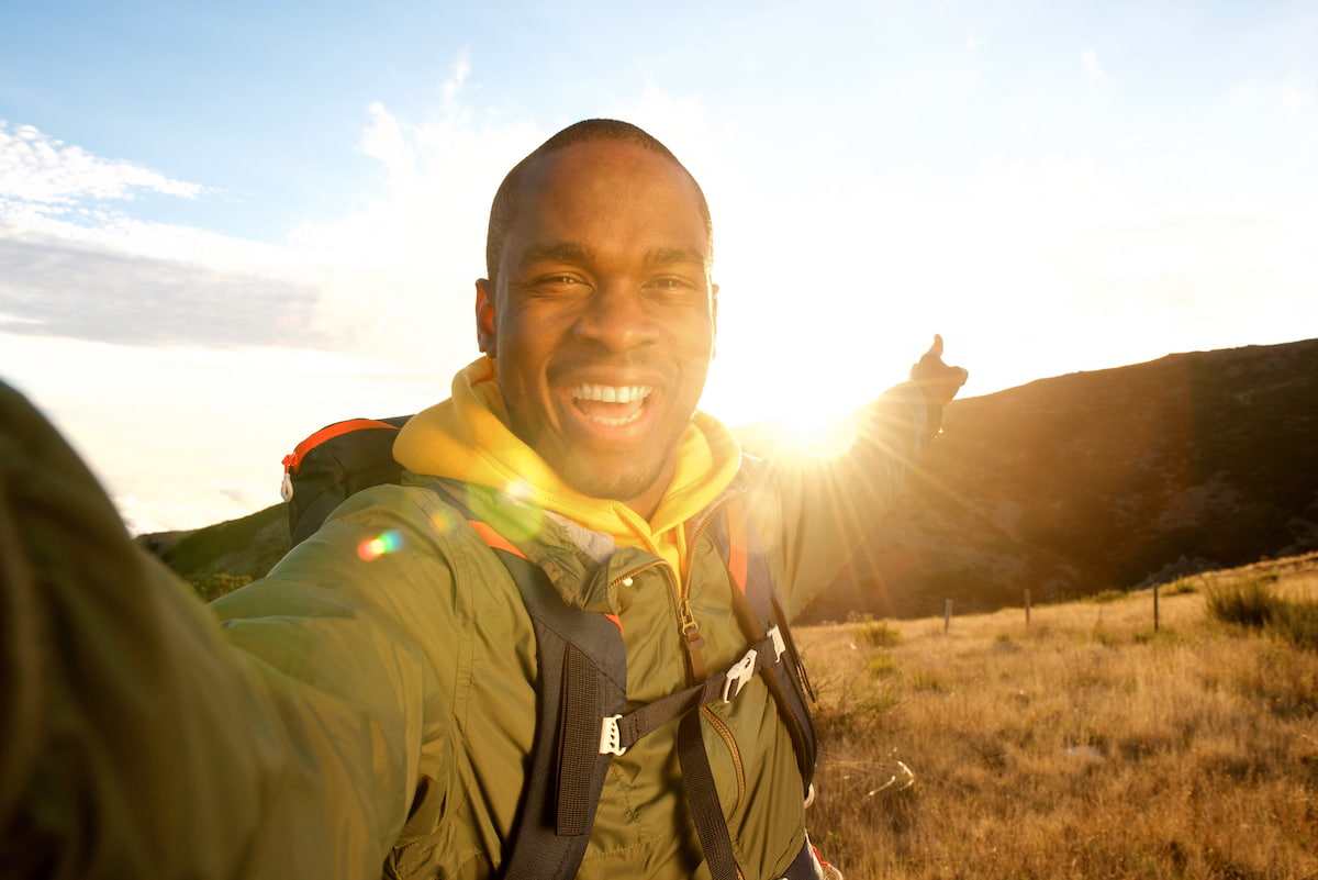 young man hiking at sunset and smiling