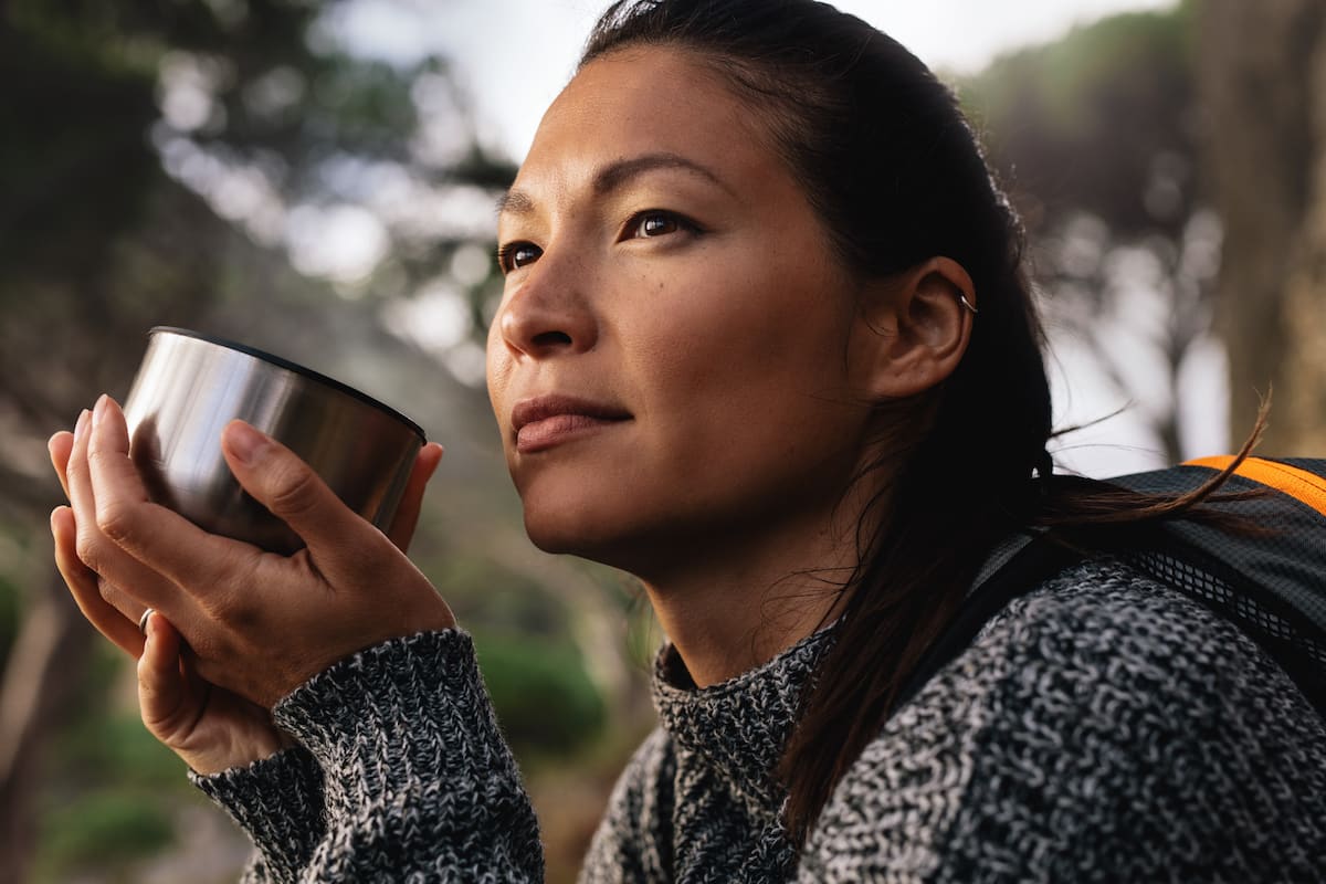 young woman drinking coffee while camping and looking into the distance