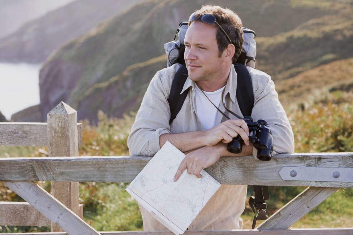 middle aged man hiking using a map and binoculars